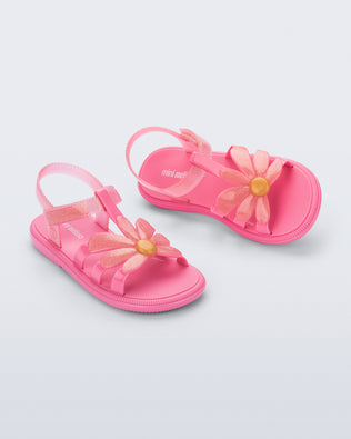 Angled view of a pair of glitter pink Hip Bloomy kids sandals with pink daisy on top