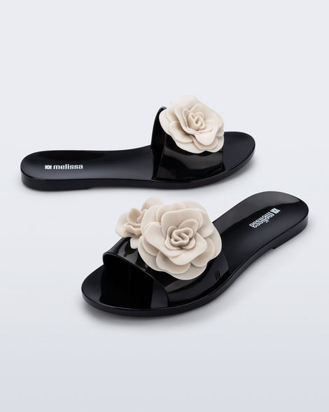 Side and angled view of a pair of black Babe Petals slide with beige flowers on top