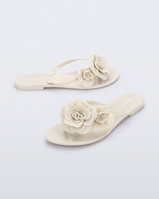 Side and angled view of a pair of beige Harmonic Petals flip Flop with beige flowers on top