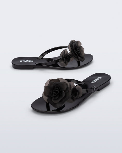 Side and angled view of a pair of black Harmonic Petals flip Flop with black flowers on top