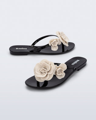Side and angled view of a pair of black Harmonic Petals flip Flop with beige flowers on top