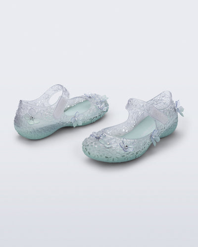 Back and side angled view of a pair of clear Melissa + Susan Fang Luna Bloom flats with flower adornments and misty green sole