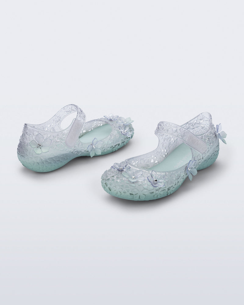 Back and side angled view of a pair of clear Melissa + Susan Fang Luna Bloom flats with flower adornments and misty green sole