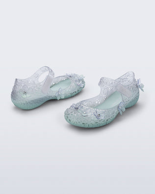 Back and side angled view of a pair of clear Melissa + Susan Fang Luna Bloom flats with flower adornments and misty green sole