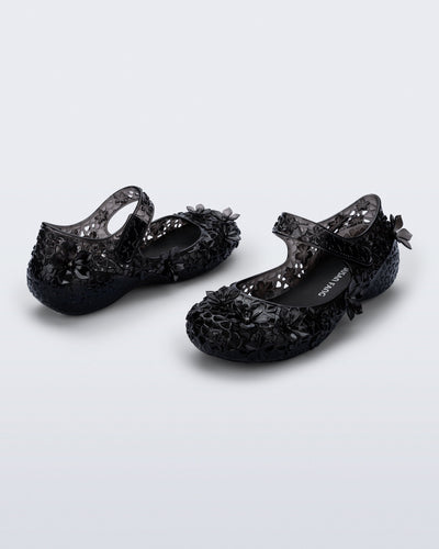 Back and side angled view of a pair of clear black Melissa + Susan Fang Luna Bloom flats with flower adornments 