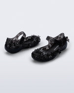 Back and side angled view of a pair of clear black Melissa + Susan Fang Luna Bloom flats with flower adornments 