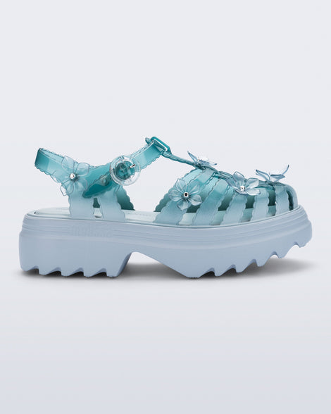 side angled view of a Clear misty blue/green Melissa + Susan Fang Possession Platform Sakura sandal with light blue soles