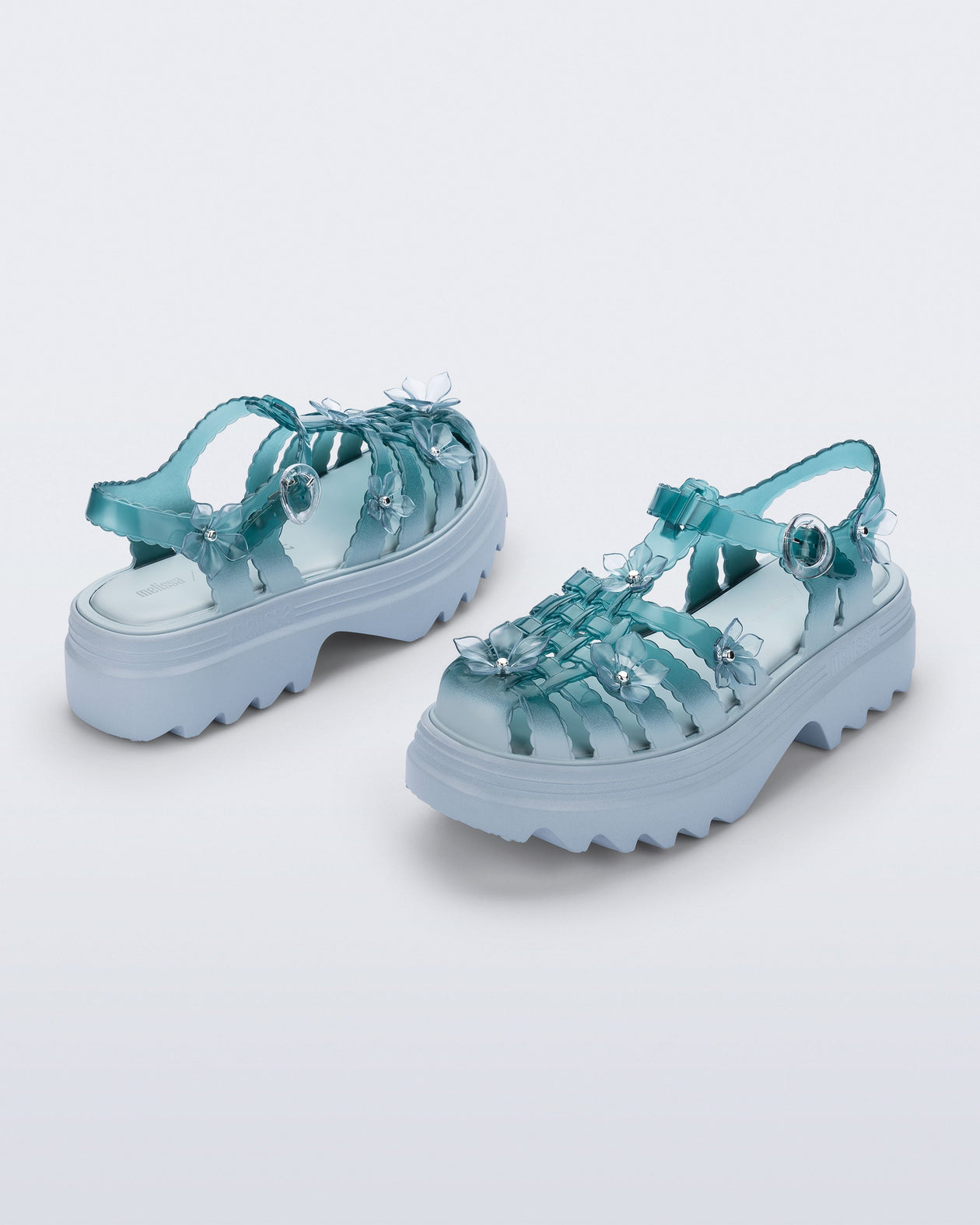 Back and side angled view of a pair of Clear misty blue/green Melissa + Susan Fang Possession Platform Sakura sandals with light blue soles