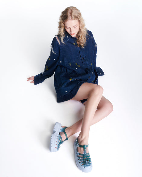 Model in a blue dress wearing a pair of Clear misty blue/green Melissa + Susan Fang Possession Platform Sakura sandals with light blue soles
