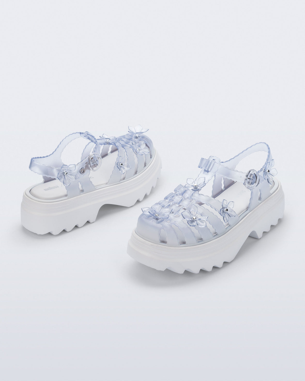 Back and side angled view of a pair of Clear Melissa + Susan Fang Possession Platform Sakura sandals with white soles