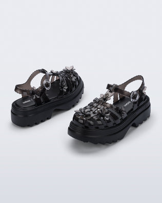 Back and side angled view of a pair of Clear black Melissa + Susan Fang Possession Platform Sakura sandals 