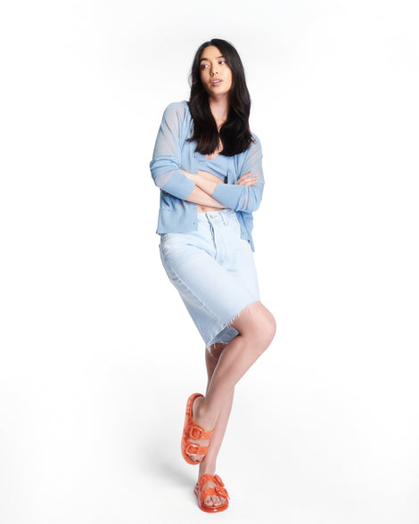 Model in a blue top and long jean shorts wearing a pair of orange Possession Slip sandals with two straps with buckles