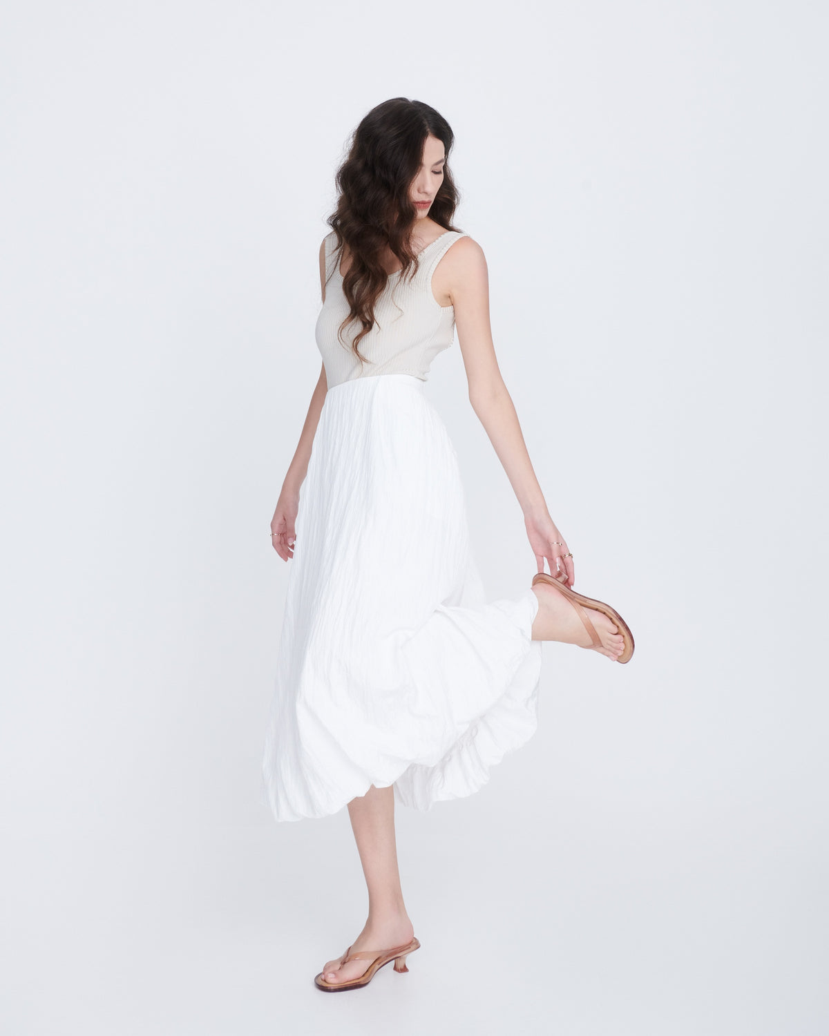 Model in a long white skirt an grey tank top wearing a pair of clear beige Flip Flop Kitten Heels