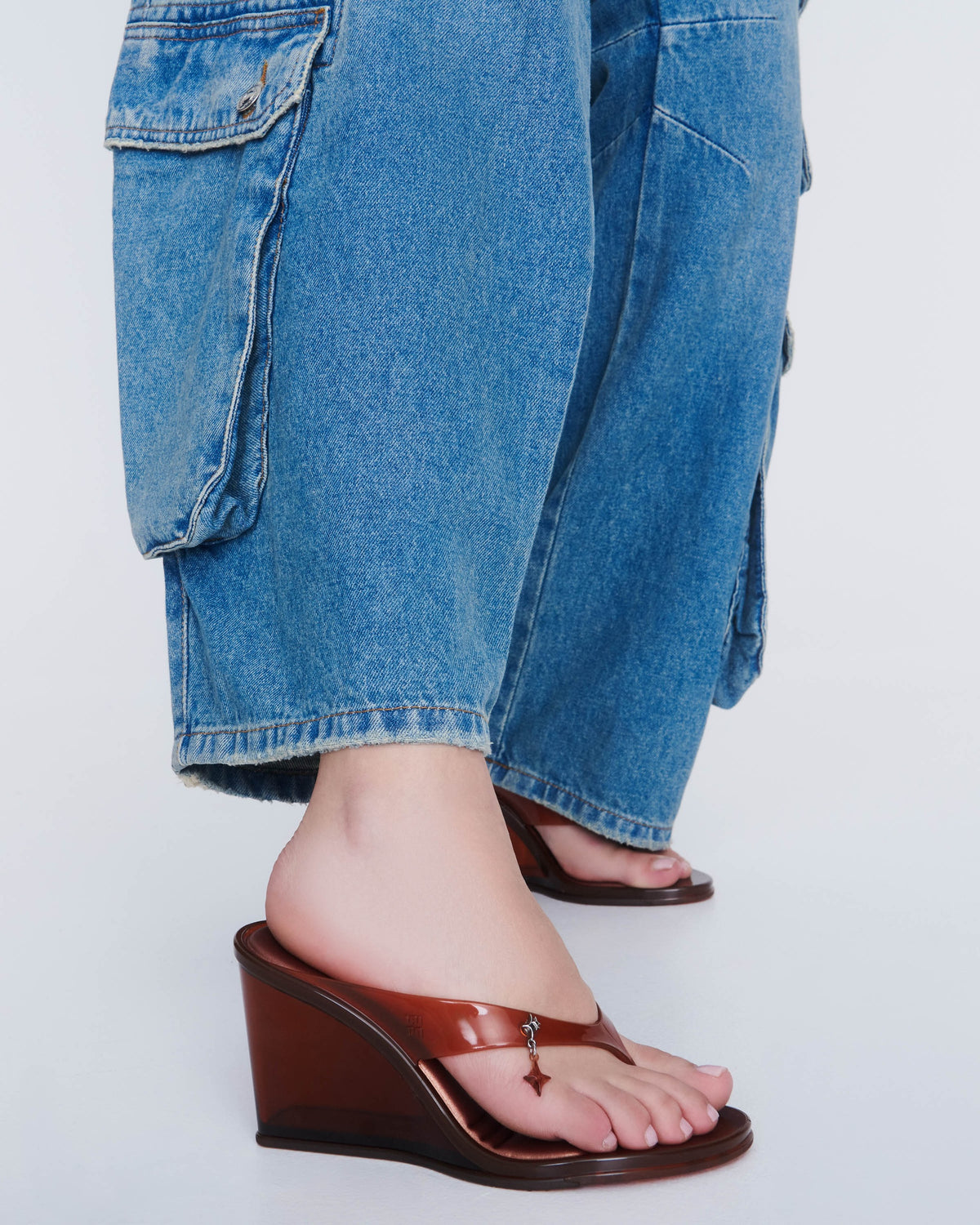 A model's legs in jeans wearing a pair of clear brown Nabeela heel wedge shoes
