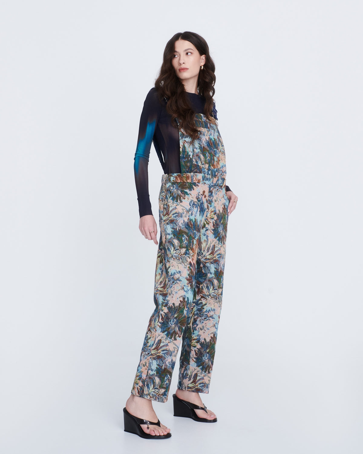 A model in a flower print overalls with a black shirt wearing a pair of black Nabeela heel wedge shoes