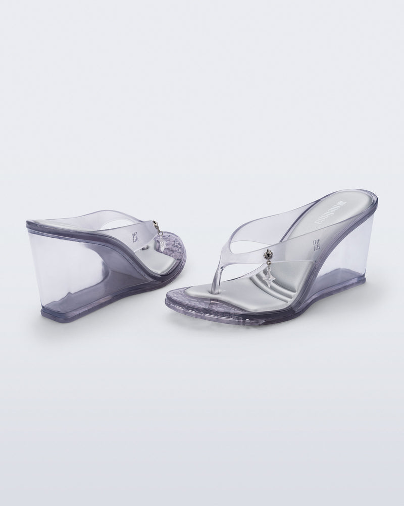 Back and angled view of a pair of clear grey Nabeela wedge flip flops with star charm on strap