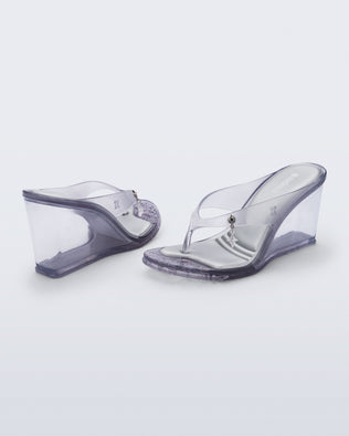 Back and angled view of a pair of clear grey Nabeela wedge flip flops with star charm on strap