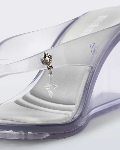 Up close view of the star charm on the strap of the clear grey Nabeela wedge flip flop