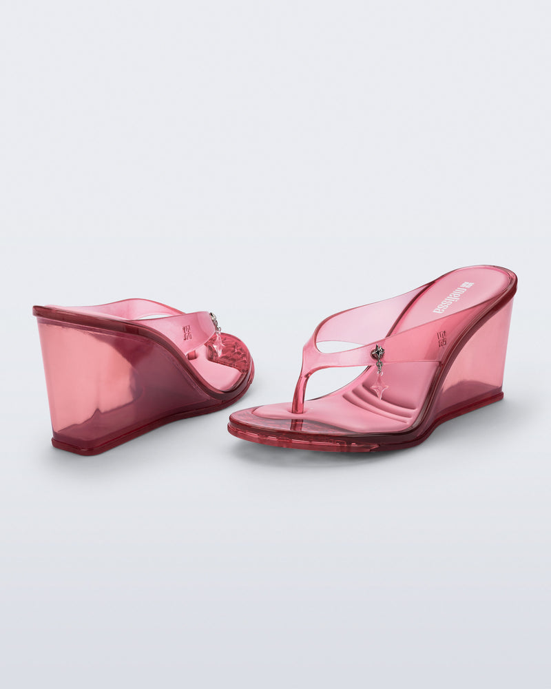 Back and angled view of a pair of pink Nabeela wedge flip flops with star charm on strap