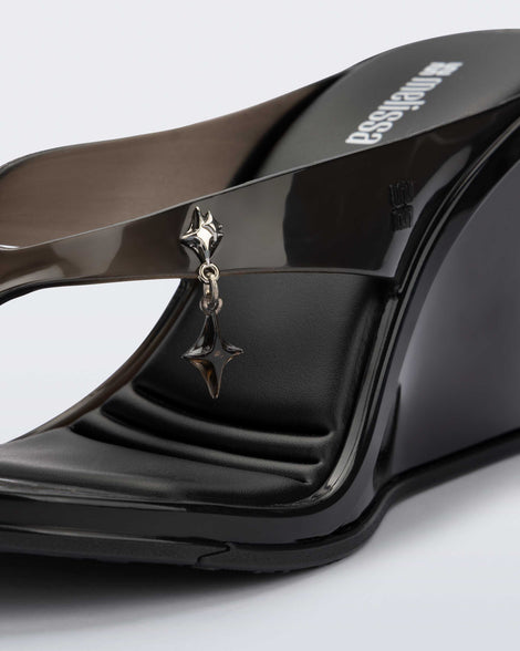 Close up of the star charm on the black Nabeela wedge flip flop.