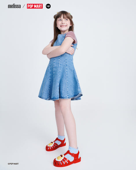 Child model in a denim dress wearing a pair of red Possession + Pop Mart Pucky kids fisherman sandals with blue socks