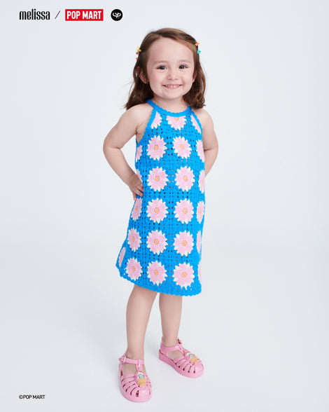 Child model in a blue dress with pink flowers wearing a pair of pink Possession + Pop Mart Pucky baby fisherman sandals