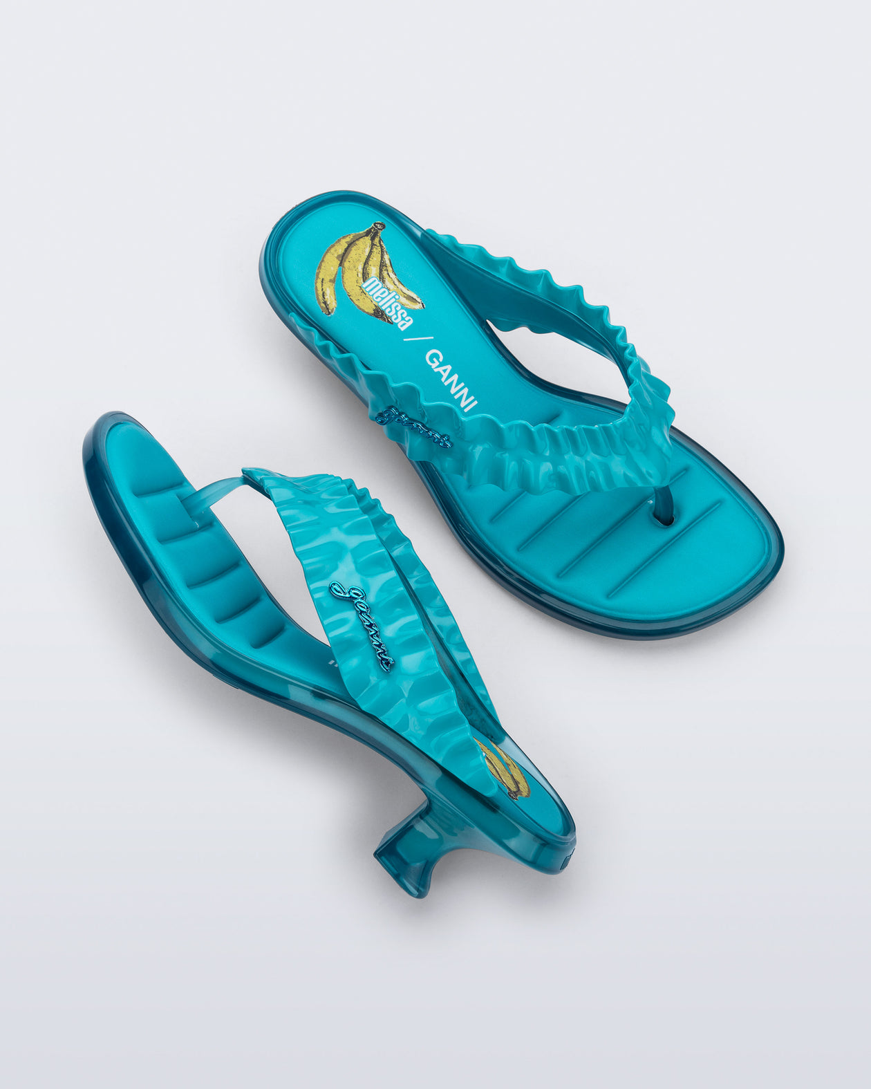 Top and side view of a pair of blue Flip Flop Kitten Heel + GANNI sandals with Banana print foot bed and faux ruffle strap
