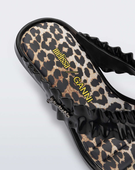 Close up angled view of a black Flip Flop Kitten Heel + GANNI sandal with leopard print foot bed and faux ruffle strap