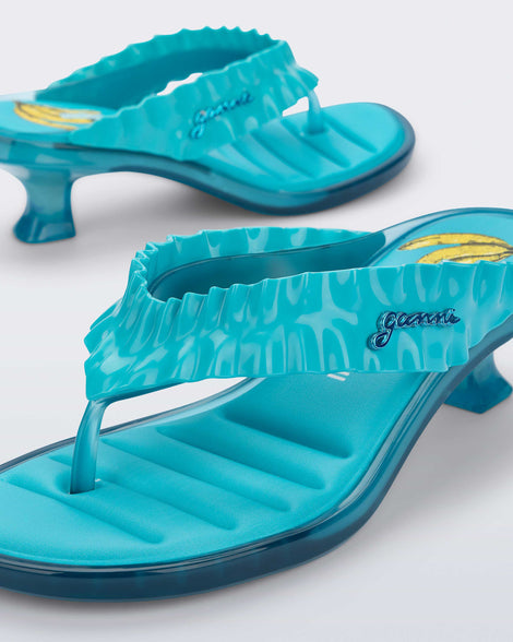 Close up angled  view of a pair of blue Flip Flop Kitten Heel + GANNI sandals with Banana print foot bed and faux ruffle strap