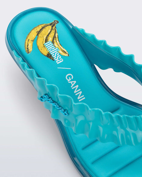 Close up view of the heel of a blue Flip Flop Kitten Heel + GANNI sandal with Banana print foot bed and faux ruffle strap
