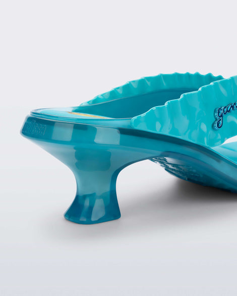 Close up view of the back heel of a blue Flip Flop Kitten Heel + GANNI sandal with Banana print foot bed and faux ruffle strap