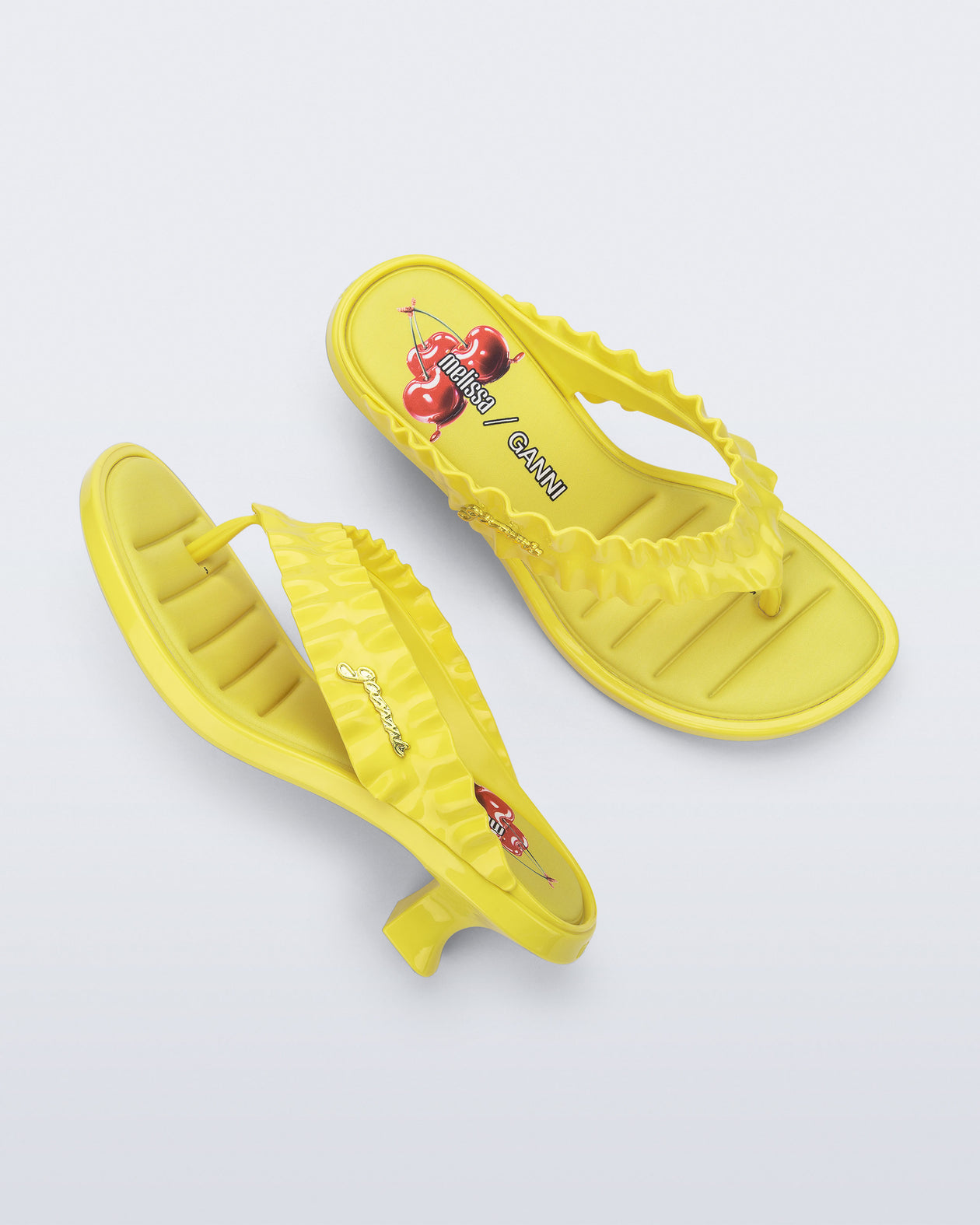 Top and side view of a pair of yellow Flip Flop Kitten Heel + GANNI sandals with cherry print foot bed and faux ruffle strap