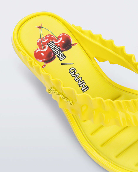 Close up view of the heel of a  yellow Flip Flop Kitten Heel + GANNI sandal with cherry print foot bed and faux ruffle strap