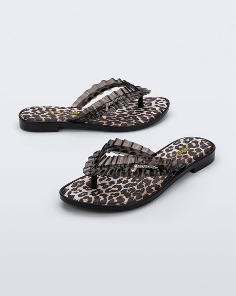 Side and angled view of a pair of black Flip Flop Slim + GANNI sandals with leopard print foot bed and faux ruffle strap
