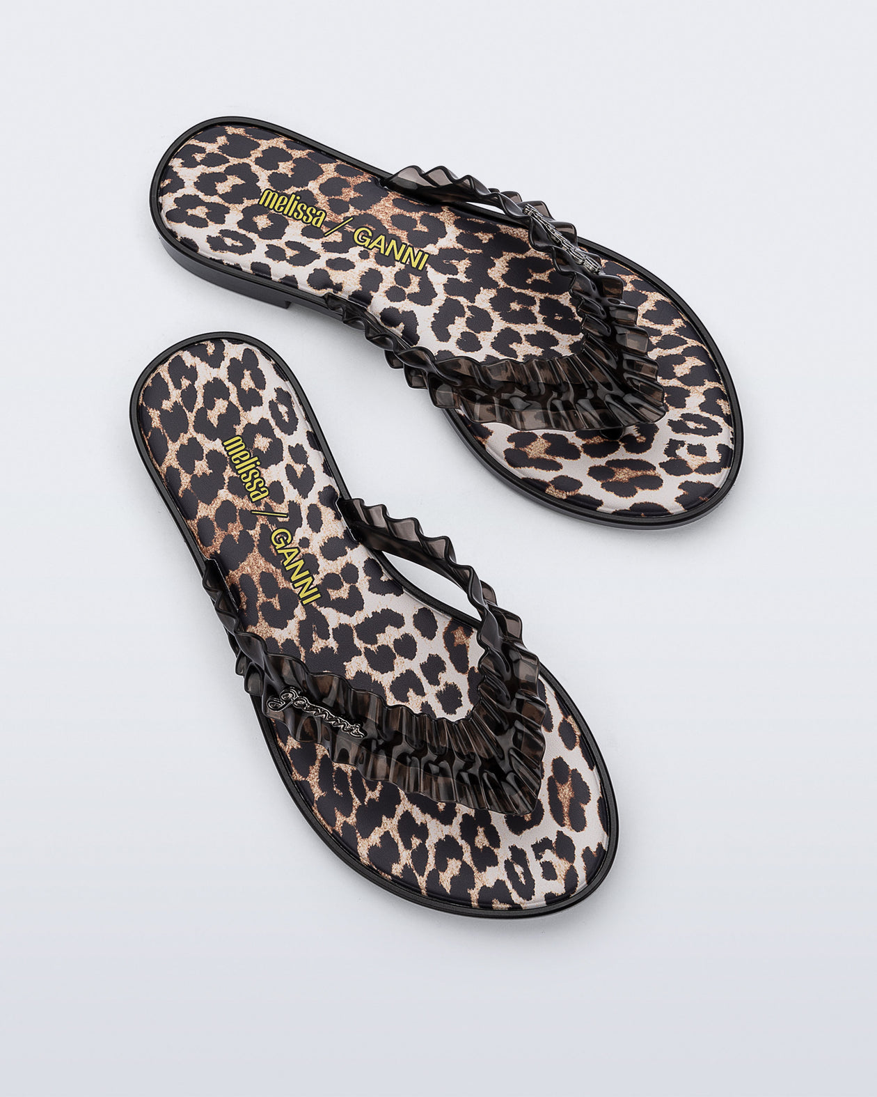 Top view of a pair of black Flip Flop Slim + GANNI sandals with leopard print foot bed and faux ruffle strap