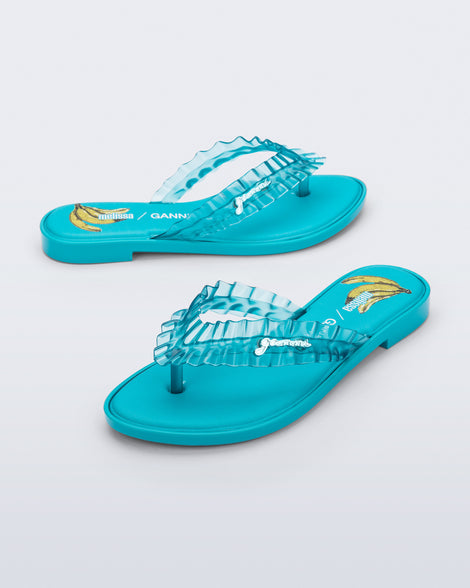 Side and angled view of a pair of blue Flip Flop Slim + GANNI sandals with a banana print foot bed and faux ruffle strap