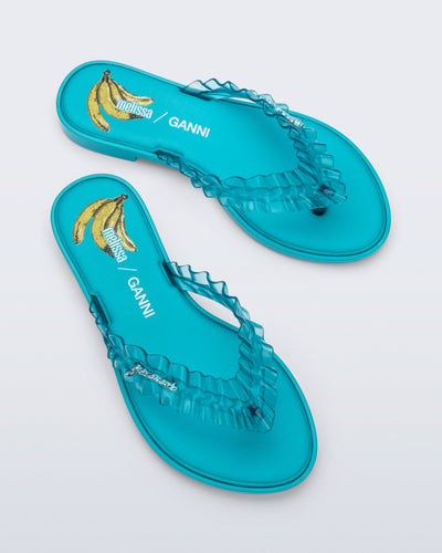 Top view of a pair of blue Flip Flop Slim + GANNI sandals with a banana print foot bed and faux ruffle strap