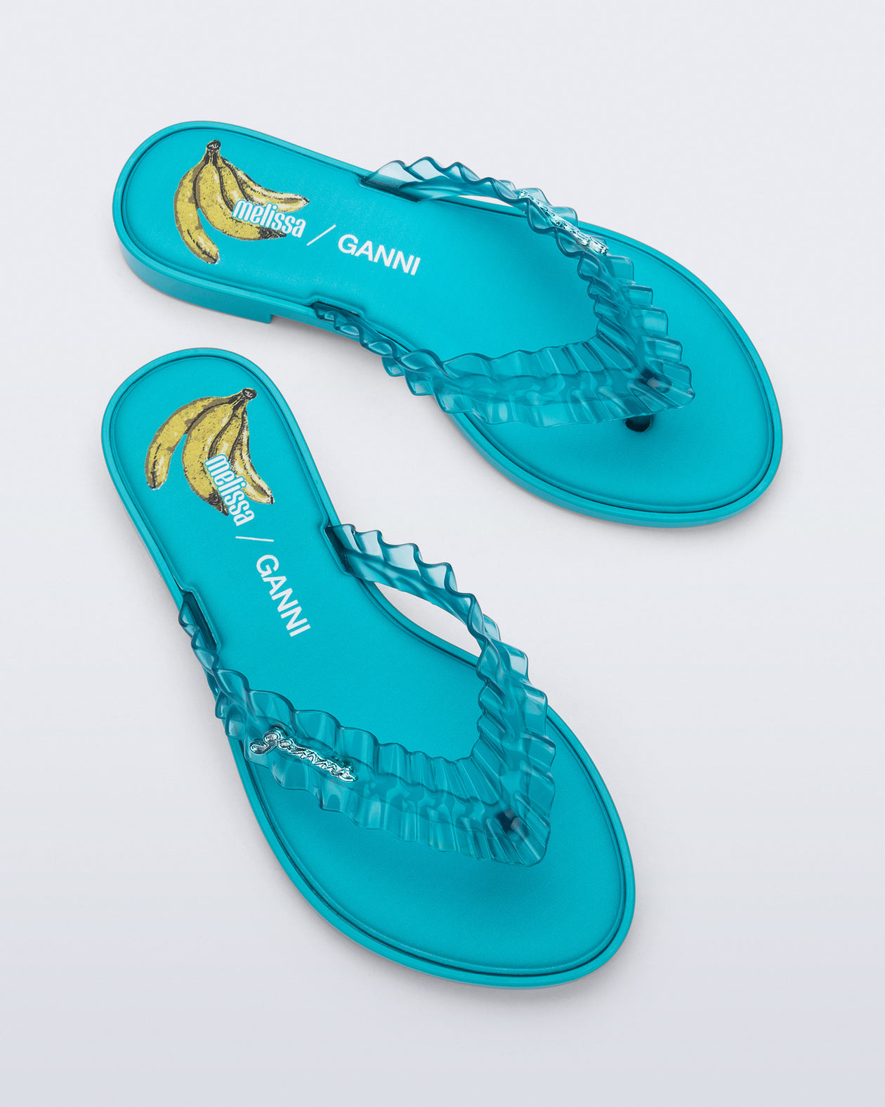Top view of a pair of blue Flip Flop Slim + GANNI sandals with a banana print foot bed and faux ruffle strap