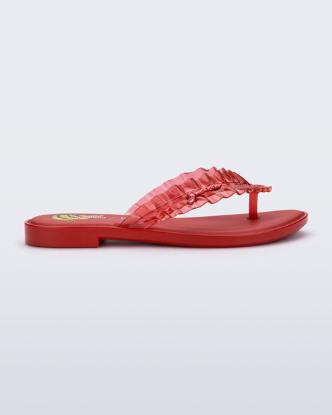 Side view of a red Flip Flop Slim + GANNI sandal with a banana print foot bed and faux ruffle strap