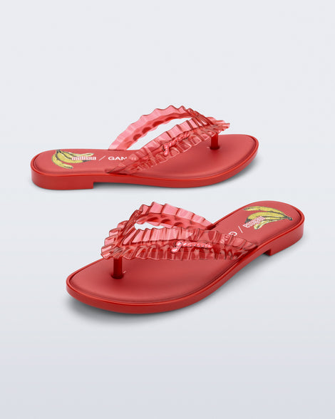 Side and angled view of a red Flip Flop Slim + GANNI sandals with a banana print foot bed and faux ruffle strap