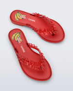 Top view of a pair of red Flip Flop Slim + GANNI sandals with a banana print foot bed and faux ruffle strap