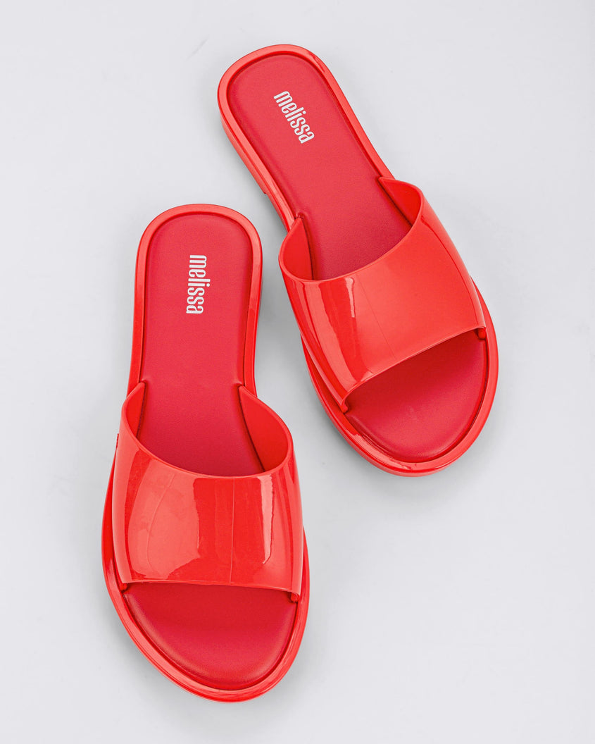 A top view of a pair of red tortoiseshell Melissa Miranda slides