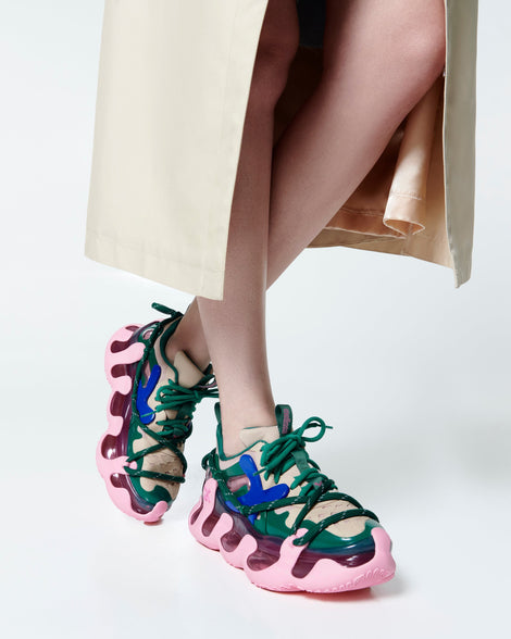 Model's legs in a pair of Melissa X Icon sneaker with pink sole and green and blue accents