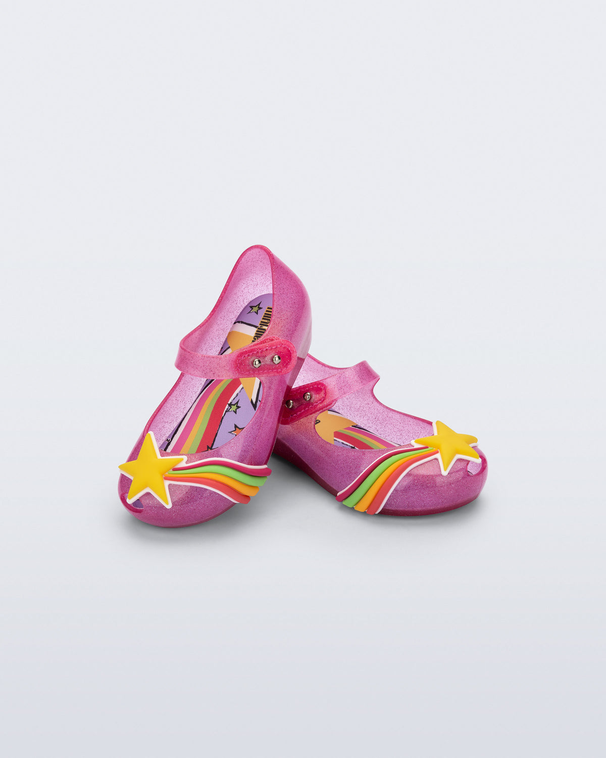 Angled view of a pair of glitter pink Ultragirl Colors baby flats with yellow star and rainbow on top