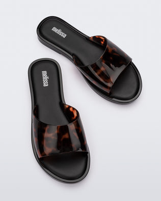 An angled top view of a pair of black tortoiseshell Melissa Miranda slides