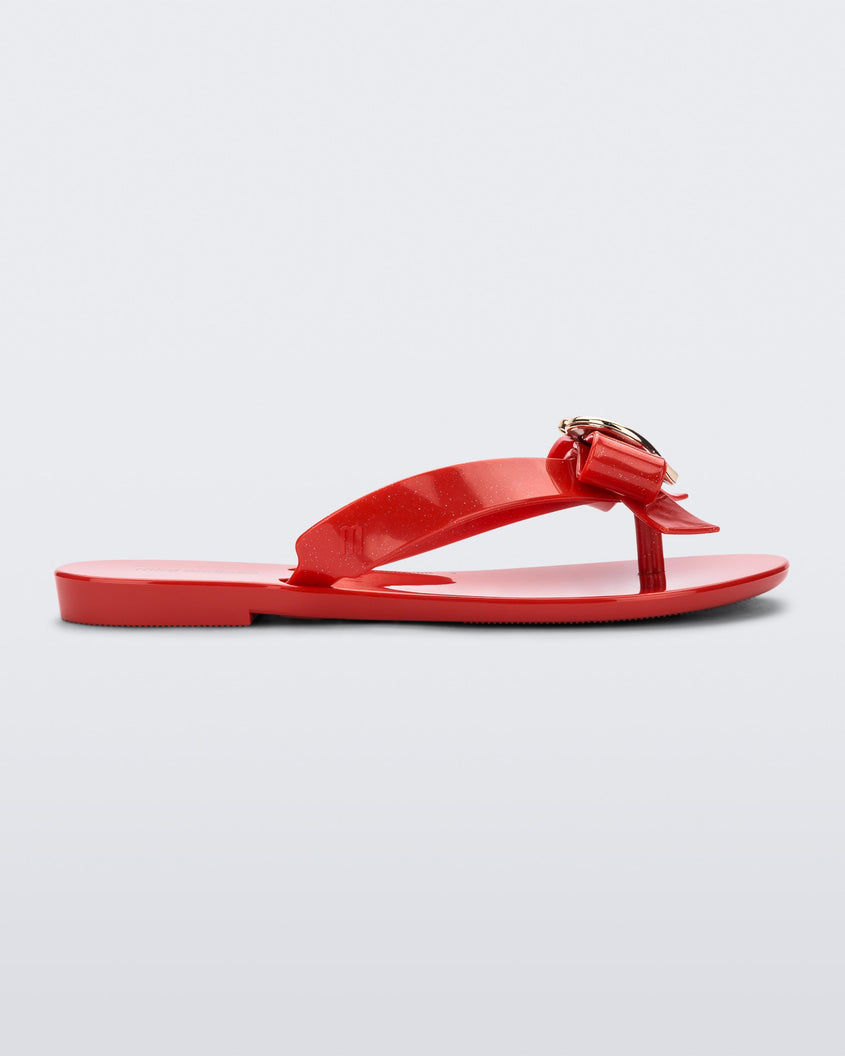 Side view of a red Mini Melissa Harmonic Heart flip flop with a red bow and gold heart detail on the straps