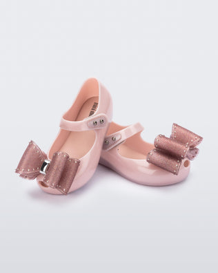Angled view of a pair of light pink Ultragirl Classic bow baby flats with glitter pink bow