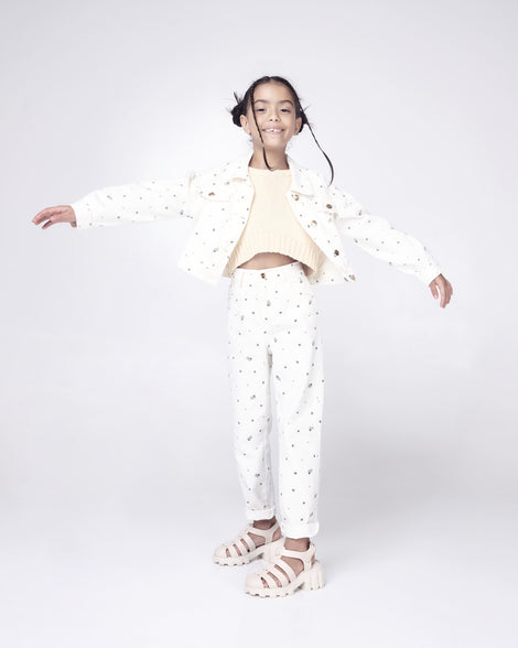 Child model in a white outfit wearing a pair of beige Megan kids heel sandals.