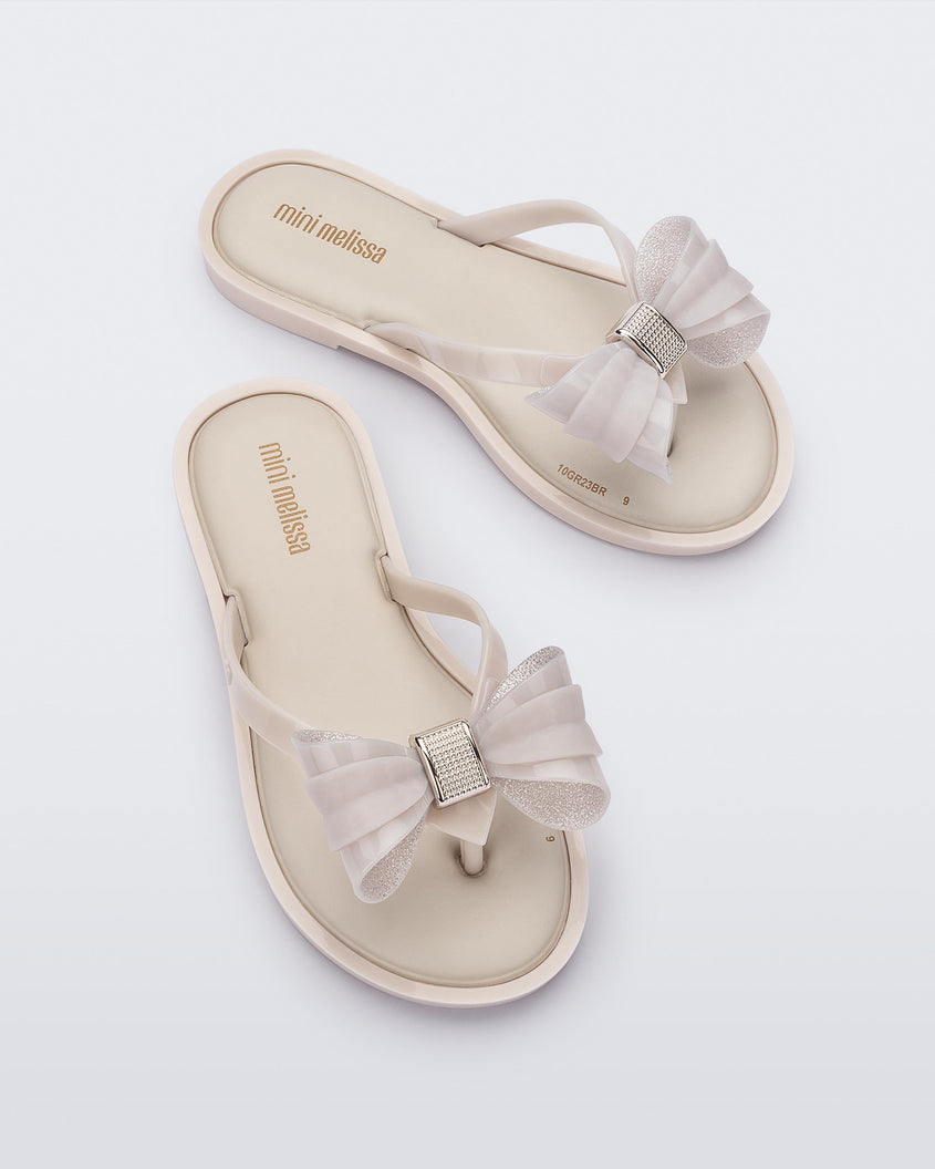 Overhead view of a pair of Mini Melissa Flip Flops in beige with bow applique