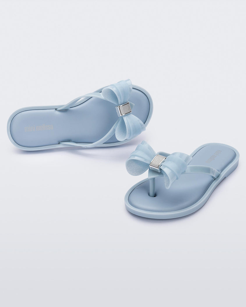 Angled view of a pair of Mini Melissa Flip Flops in blue with bow applique